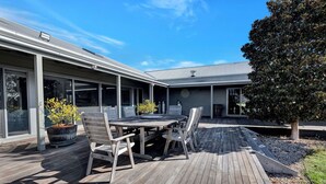 A modern house with a wooden deck, a dining table with chairs, and a potted plant.