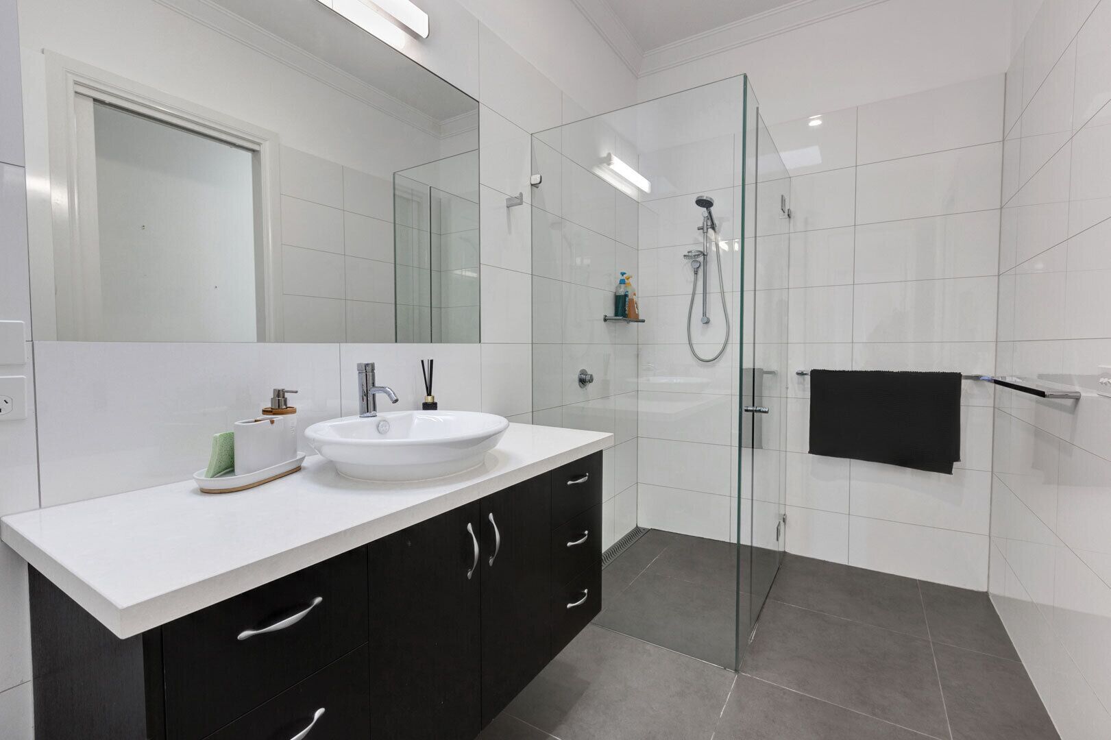 A modern bathroom with a white sink, dark cabinets, a glass shower enclosure, and a black towel rack.