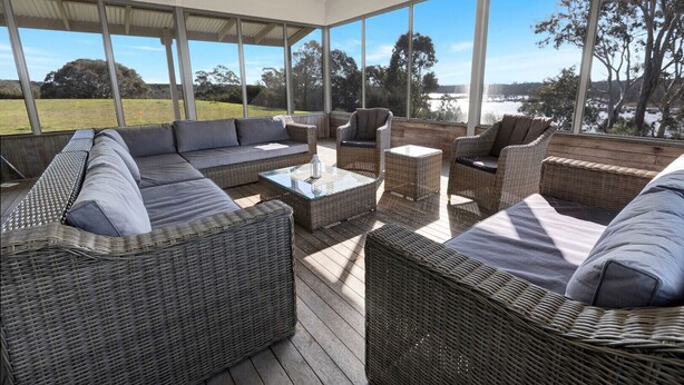 A covered outdoor seating area with wicker furniture and a glass table, overlooking a natural landscape.