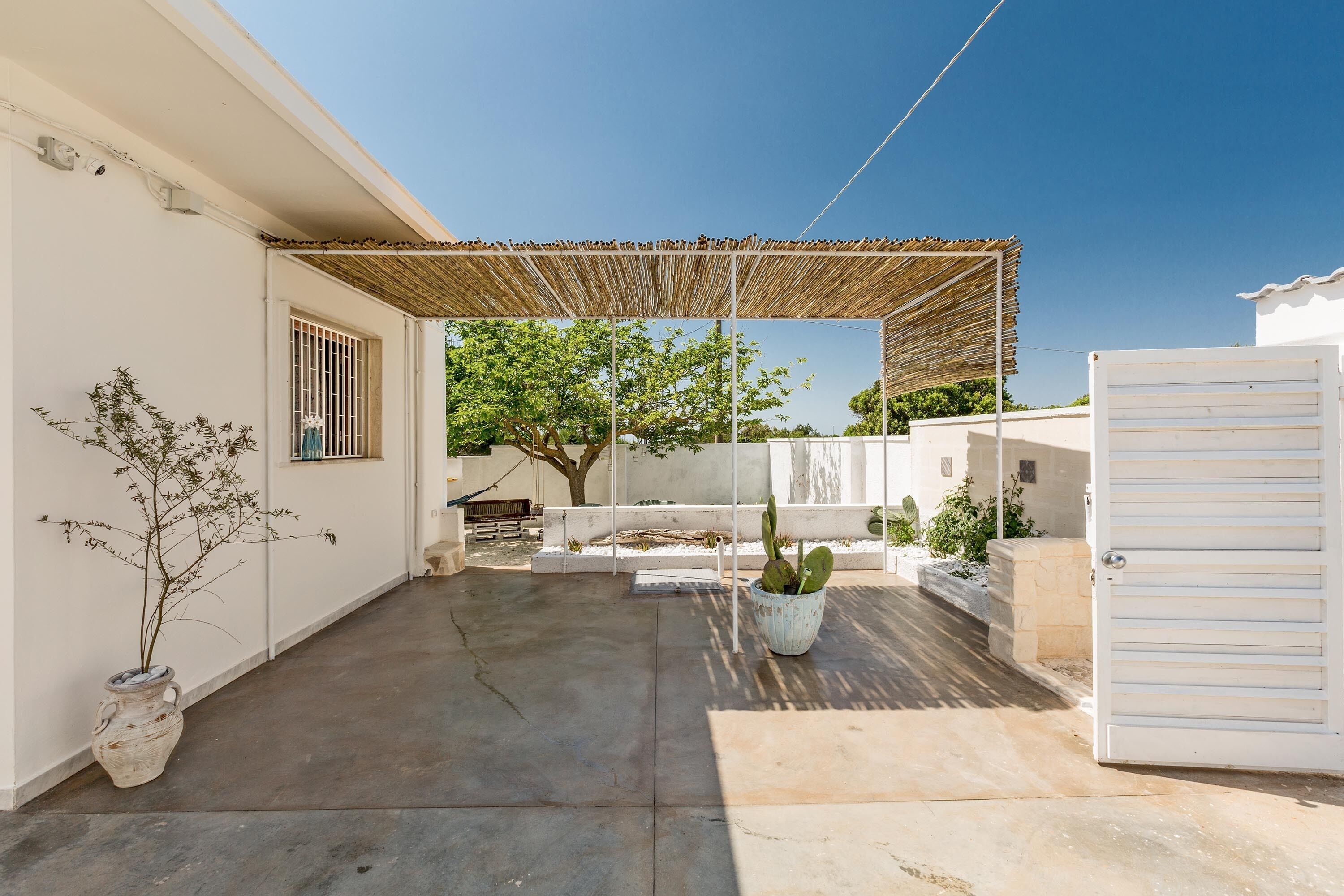A covered patio area with a concrete floor, potted plants, and a white gate.