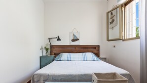 A bedroom with a wooden headboard, a bed with a patterned bedspread, a bedside table with a lamp, and a wall-mounted sailboat decoration. - 3490 Villetta Boschetto by Barbarhouse (Maruggio)