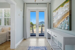 A hallway with a white console table, a door with a view, and a tiled floor.