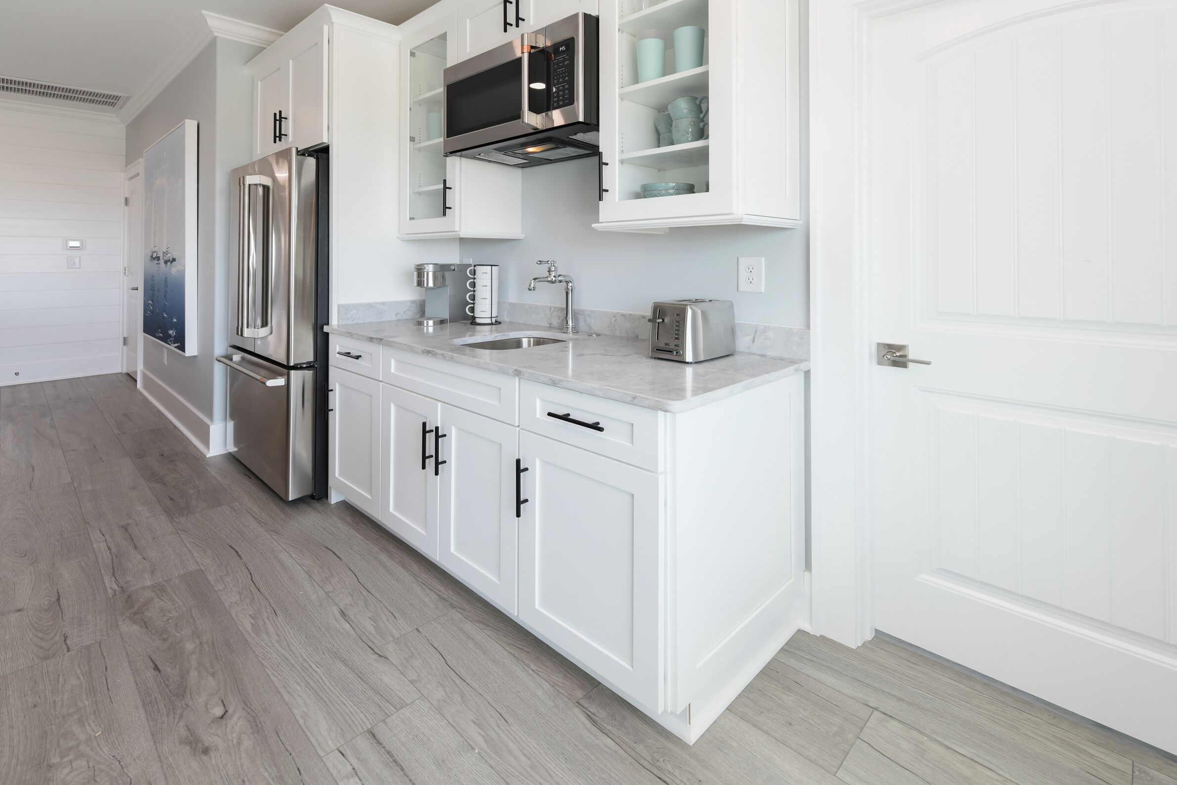 A modern kitchen with white cabinetry, stainless steel appliances, and a marble countertop.