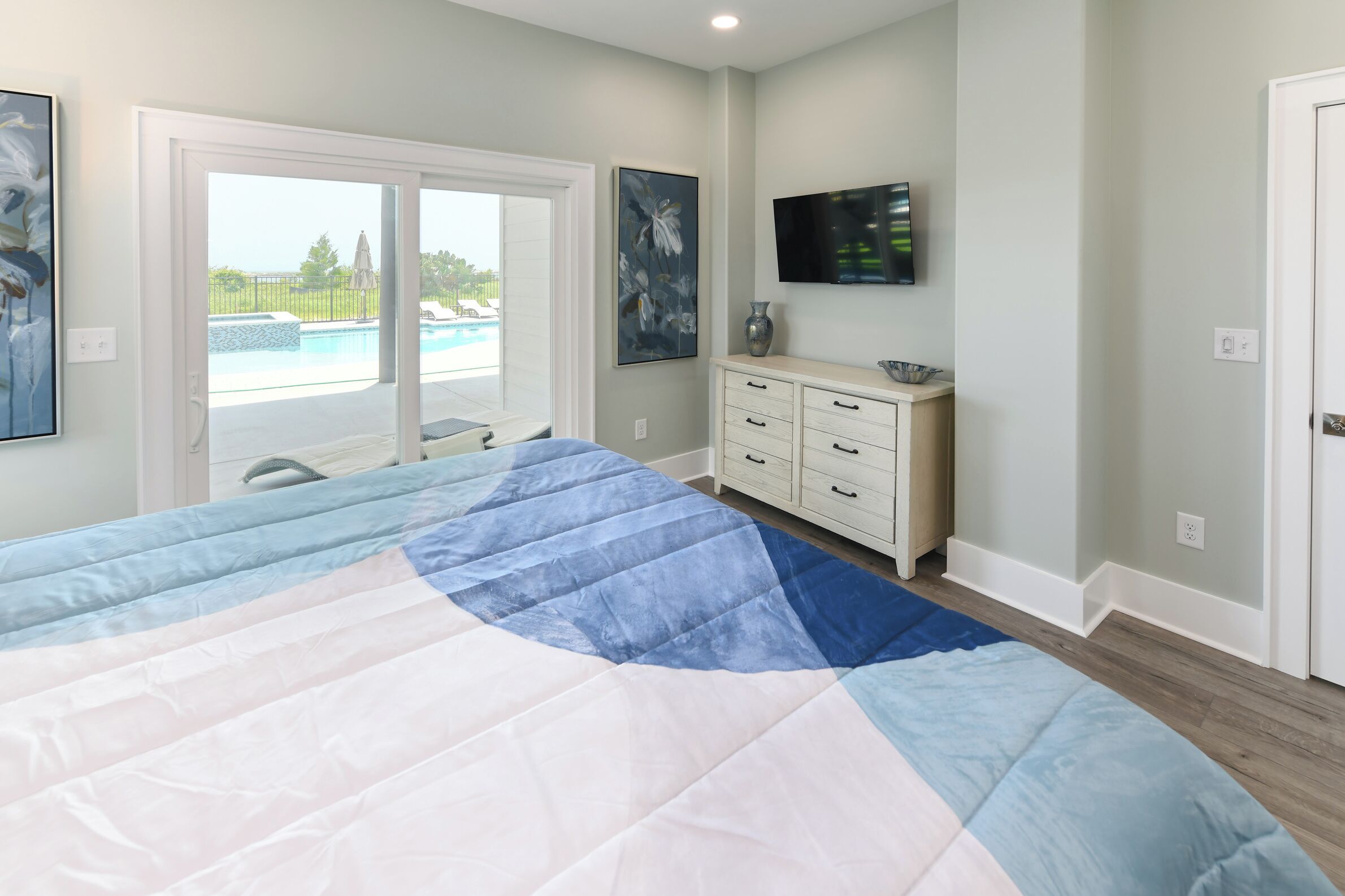 Een slaapkamer met een groot bed, een aan de muur bevestigde televisie en uitzicht op een zwembad door de deur.
