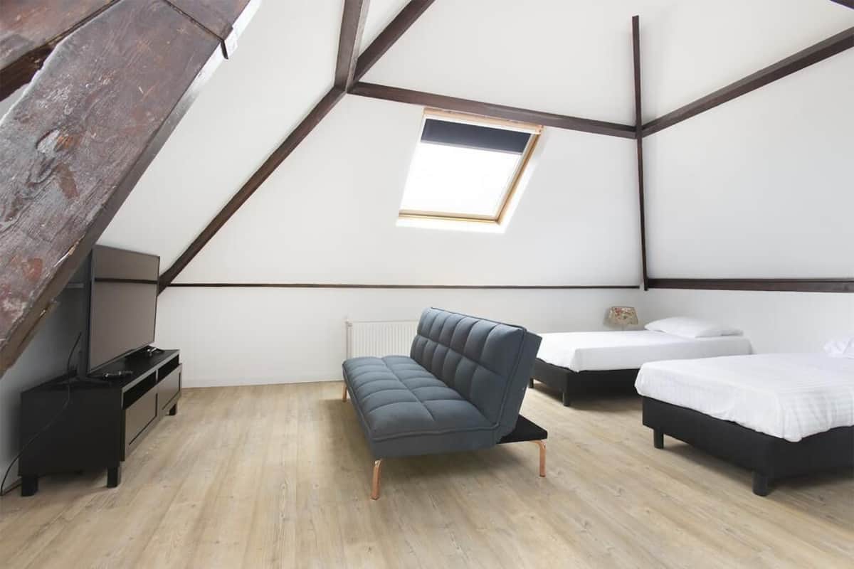 A bedroom with a sloped ceiling, a sofa, two beds, a small table, and a radiator.
