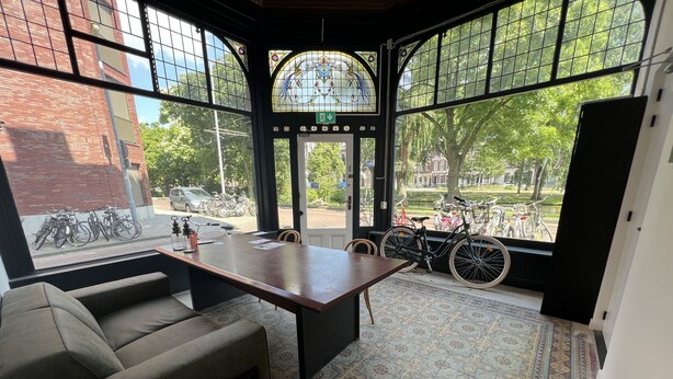 A room with a large window, a sofa, a table, and a patterned floor. - Rotterdam Inn (Rotterdam)
