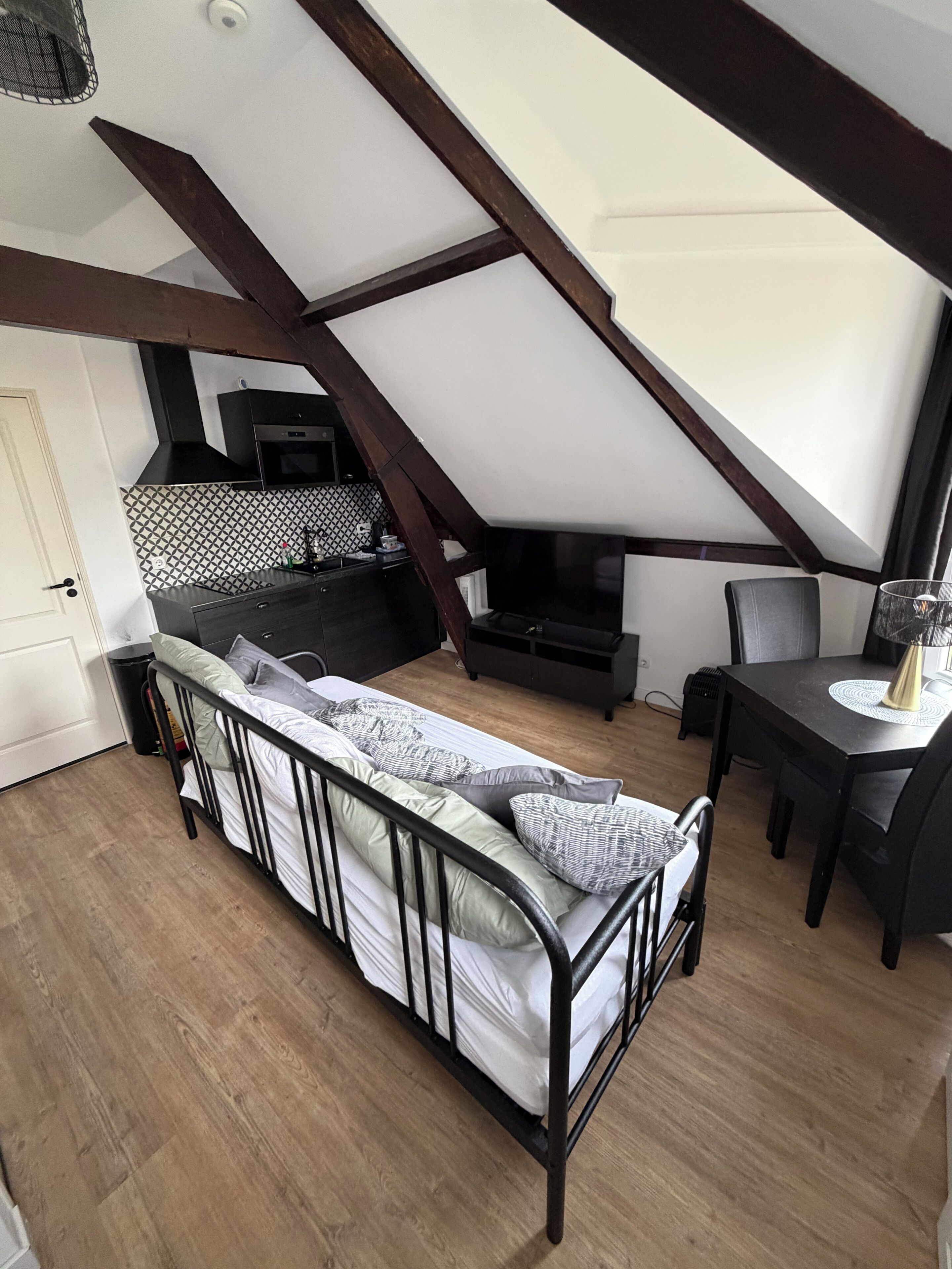 A loft bedroom with a sloped ceiling, a bed with pillows, a dining table, and a kitchen area with a microwave and sink.