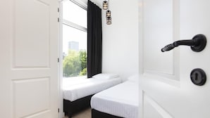 A room with two beds, a white door, and a view of greenery outside. - Rotterdam Inn (Rotterdam)