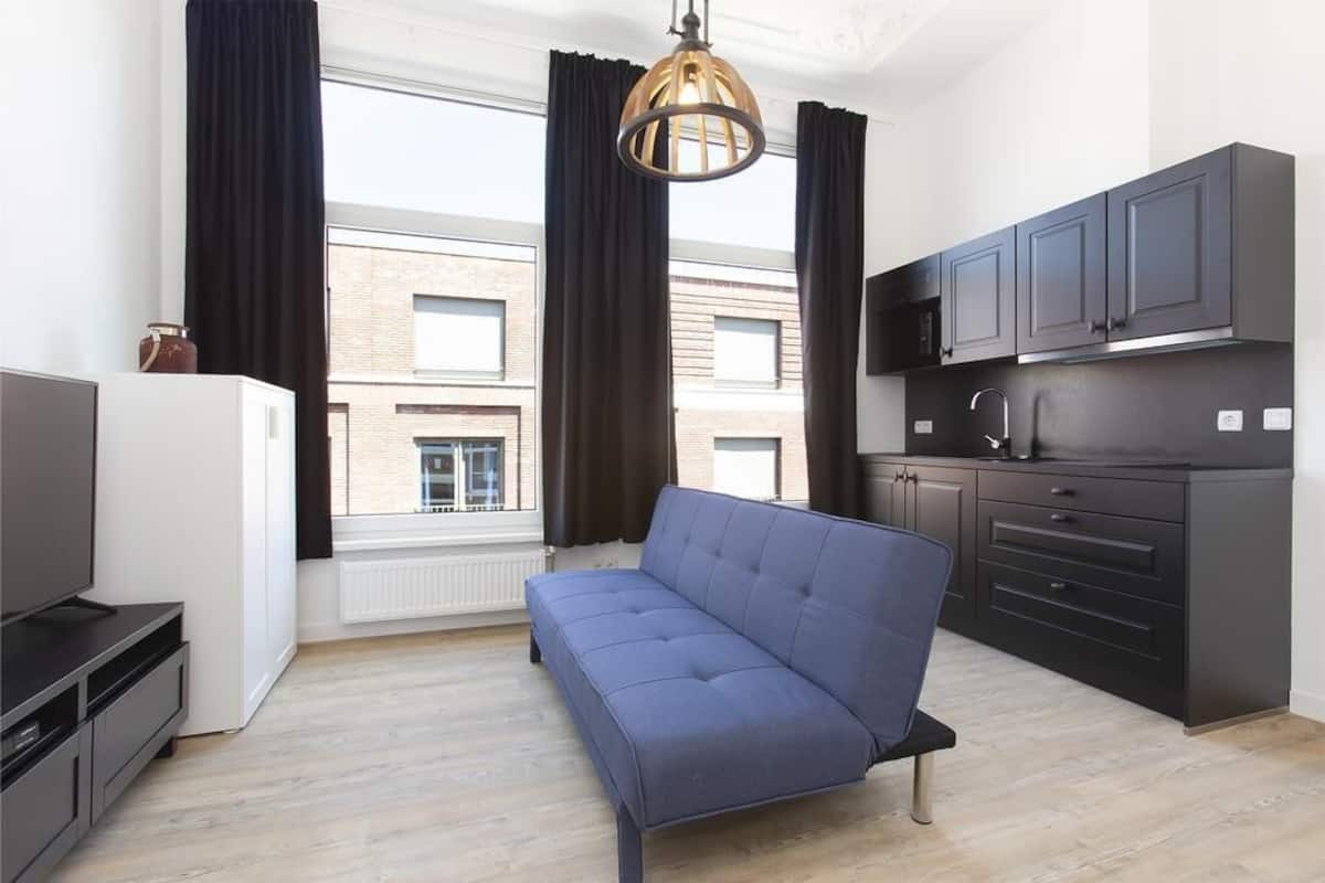 A modern apartment with a sofa, kitchen, and large windows.