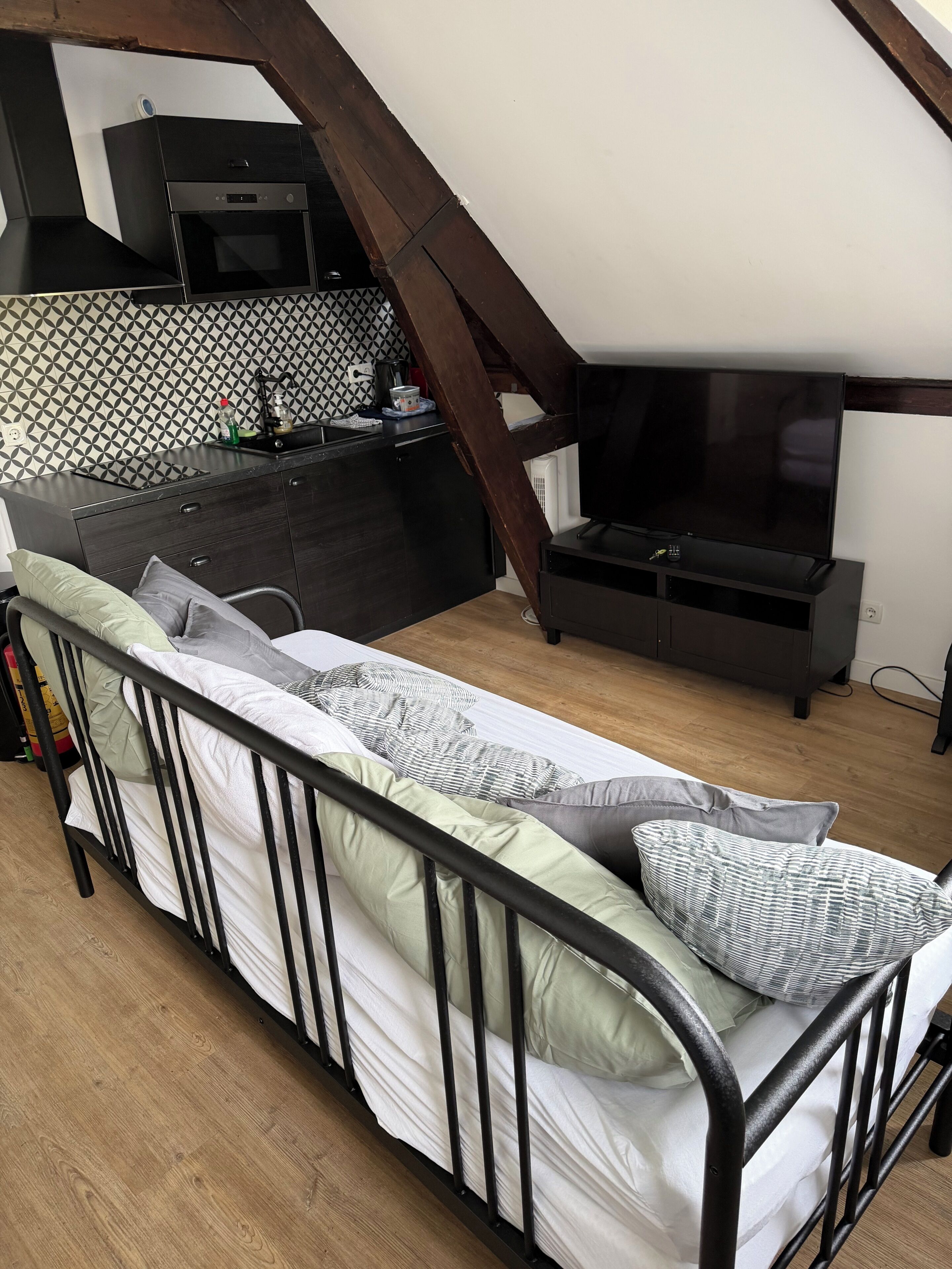 A loft bedroom with a bed, a TV, a kitchenette, and a patterned wall.