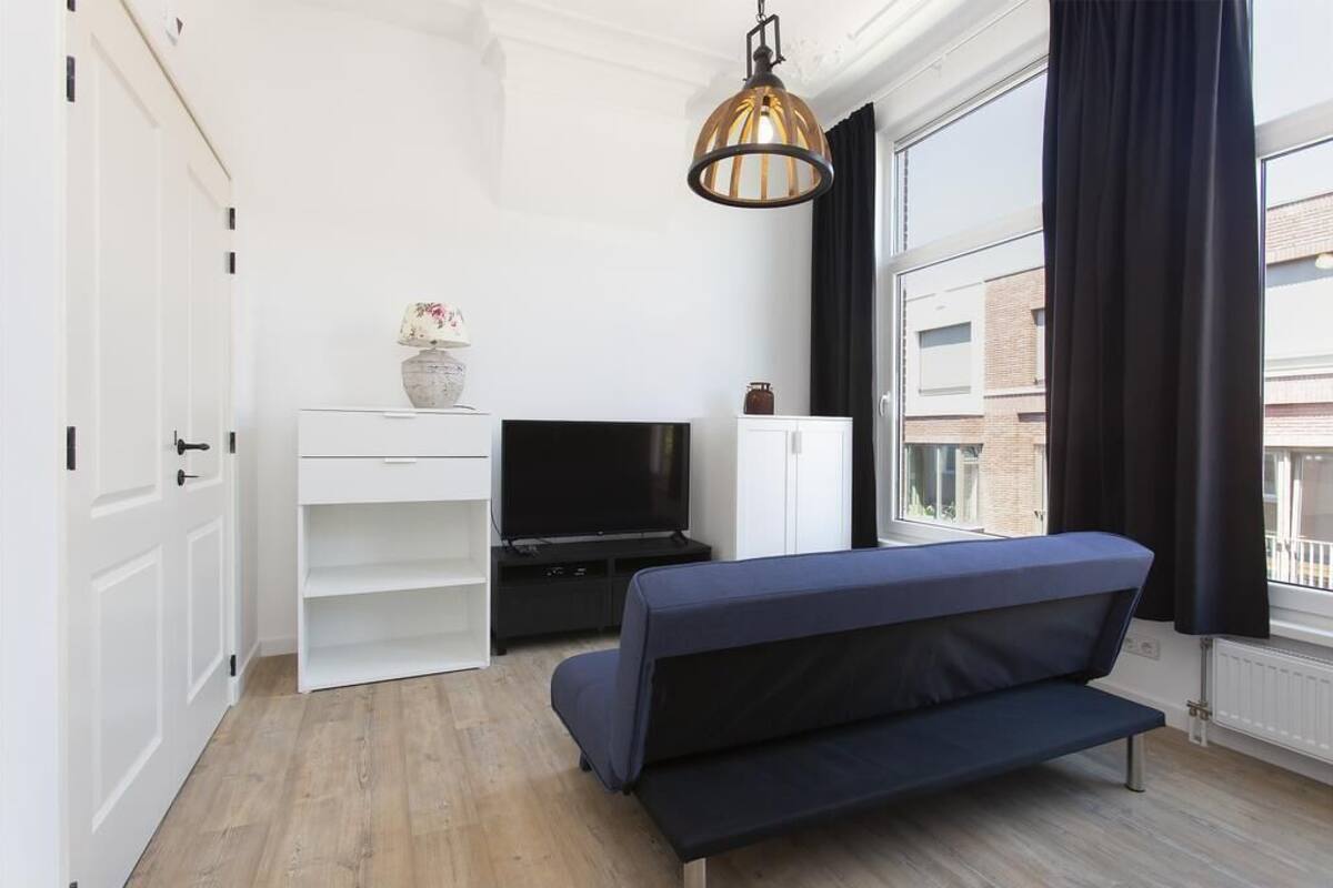 A modern living room with a sofa, TV, white cabinets, and a large window with curtains.