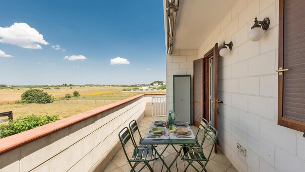 A balcony with a table set for dining, chairs, and a view of a green landscape.