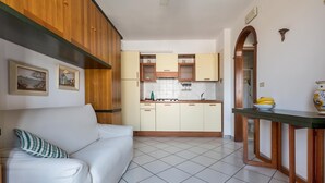 A modern kitchen with wooden cabinets, a white tiled floor, and a dining area with a glass table.