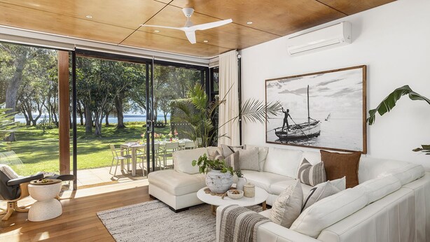 Un salón moderno con un ventanal grande, un sofá blanco, una mesita de centro y un cuadro de un barco en la pared.