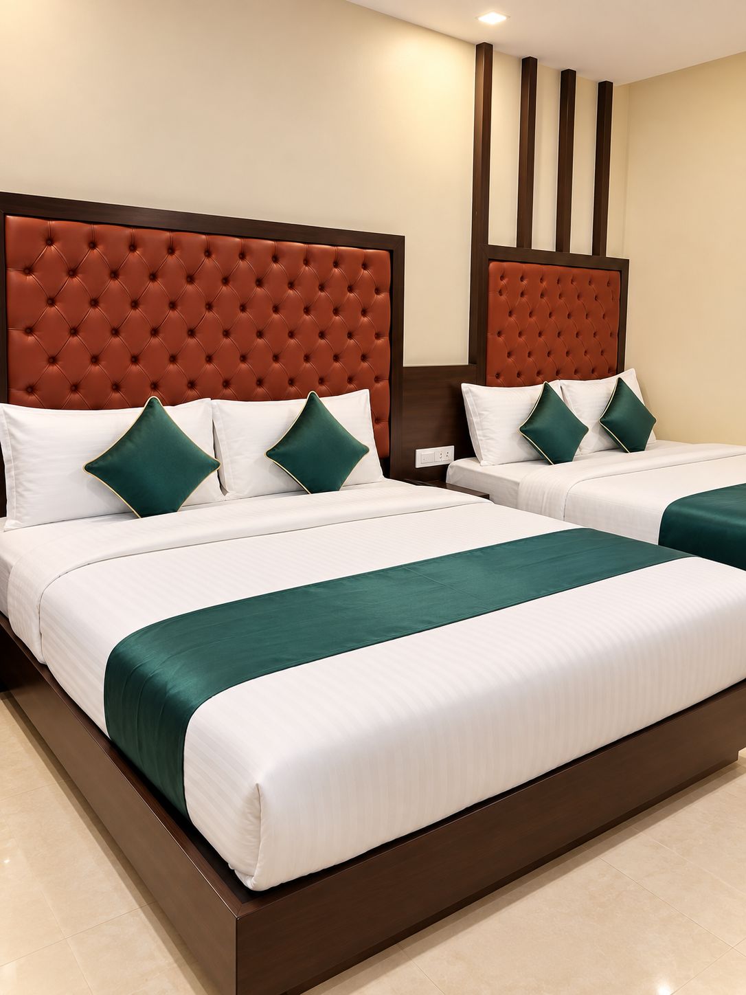 Une chambre d’hôtel avec deux lits, chacun doté d’une tête de lit capitonnée, de draps blancs et de coussins décoratifs verts.