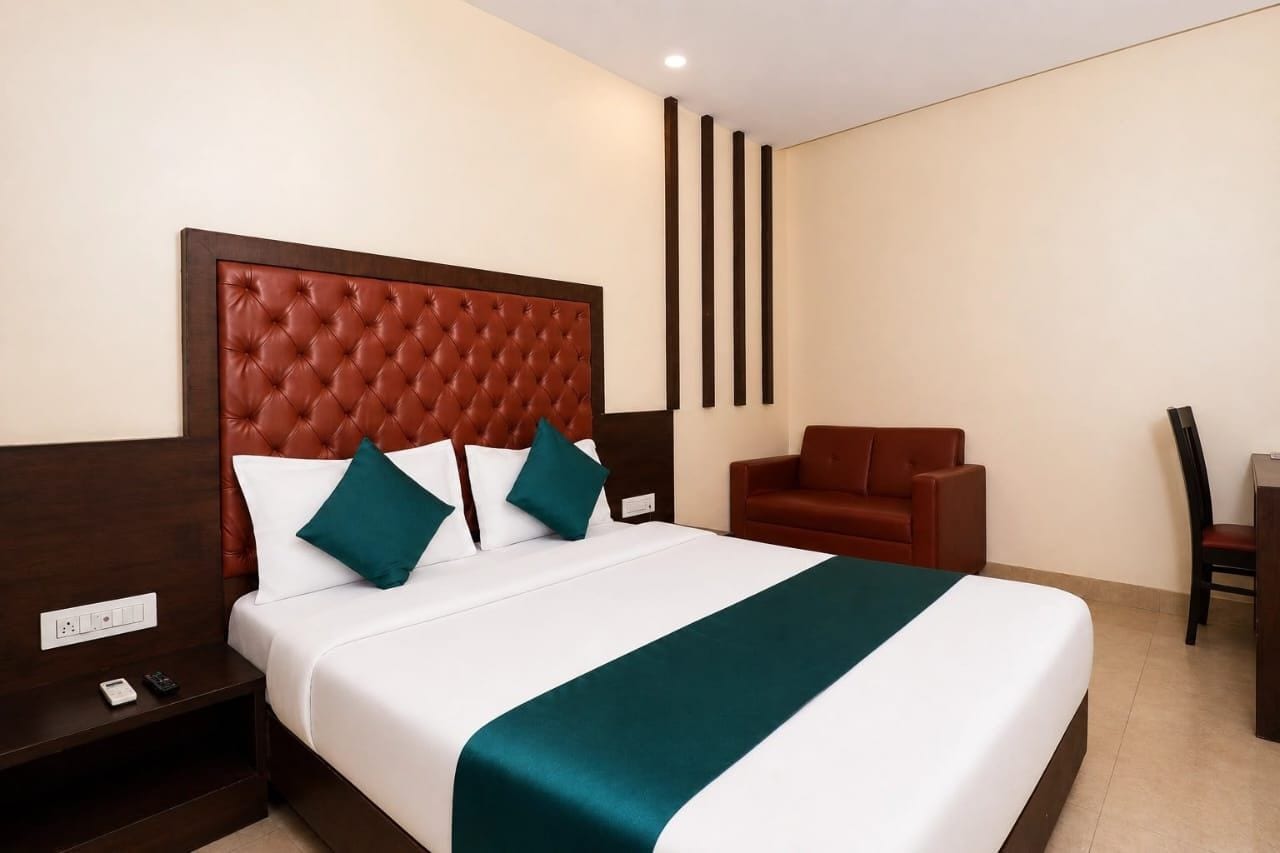 A hotel room with a large bed, a wooden nightstand, a red sofa, and a desk with a chair.