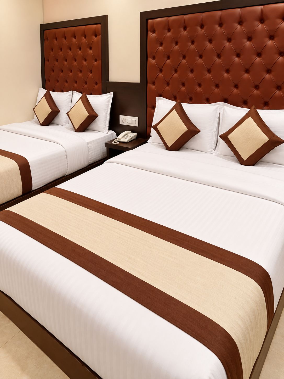 A hotel room with two beds, each with a brown headboard and white bedding. There is a nightstand with a telephone between the beds.