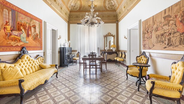Una habitación con suelo estampado, un candelabro, una mesa de comedor con sillas y obras de arte en las paredes.