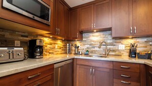 Una cocina con armarios de madera, lavavajillas de acero inoxidable, microondas, cafetera y salpicadero de piedra.