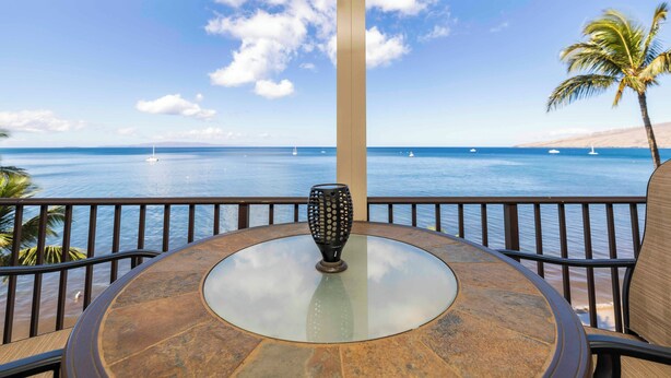 Una mesa de vidrio redonda con un jarrón decorativo en el centro, con vistas a una playa con barcos y palmeras.
