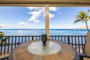 A round glass table with a decorative vase in the center, overlooking a beach with boats and palm trees. - Kihei Beach Unit 608 with Awesome Oceanfront View Unit on Sugar Beach! (Kihei)