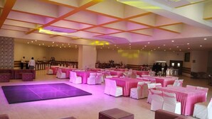 A spacious hall with a stage, rows of tables with pink tablecloths, and white chairs.