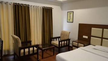Quarto de hotel com cama, duas poltronas, uma mesa pequena e uma mesinha de cabeceira.