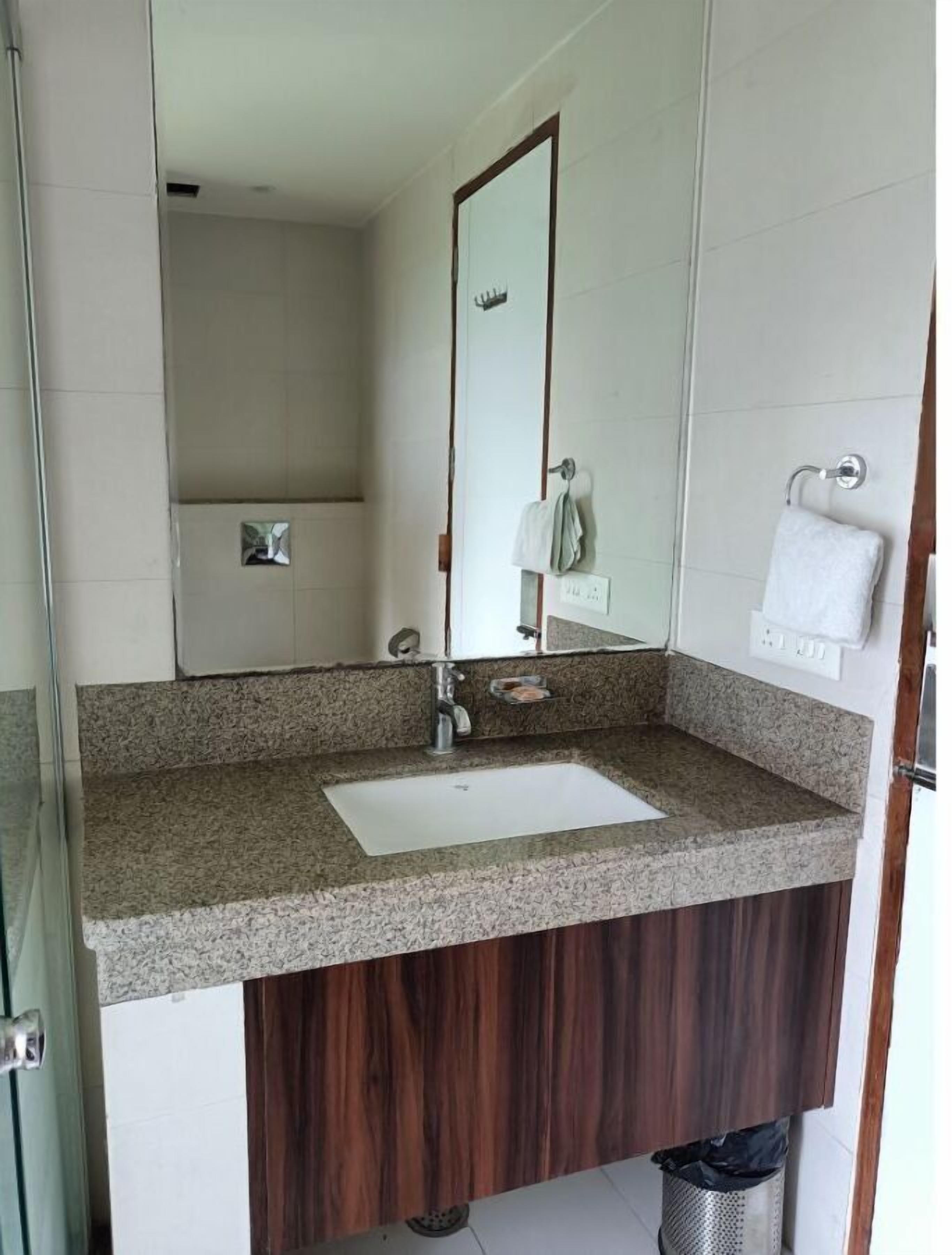 A bathroom with a granite countertop sink, a mirror, and a towel rack.