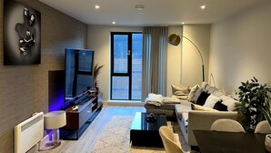A modern living room with a flat-screen TV, sofa, coffee table, and a large window with curtains. - 2-bed Luxury Apartment in Birmingham City Center (Birmingham)