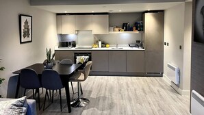A modern kitchen with grey cabinets, a dining area with a table and chairs, and a small island with a sink. - 2-bed Luxury Apartment in Birmingham City Center (Birmingham)