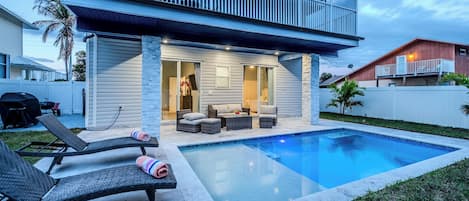 A modern house with a swimming pool, outdoor seating, and a covered patio.
