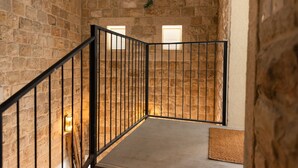 A staircase with stone walls and black railings, leading to a landing with a light fixture and a doormat. - PORT CITY HAIFA - Flea Market Luxury (Haifa)