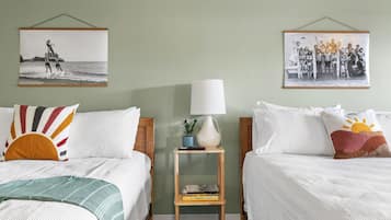 Une chambre d’hôtel avec deux lits, chacun agrémenté d’un oreiller au motif différent, une table de chevet avec une lampe et des livres, et deux tableaux encadrés accrochés au mur.