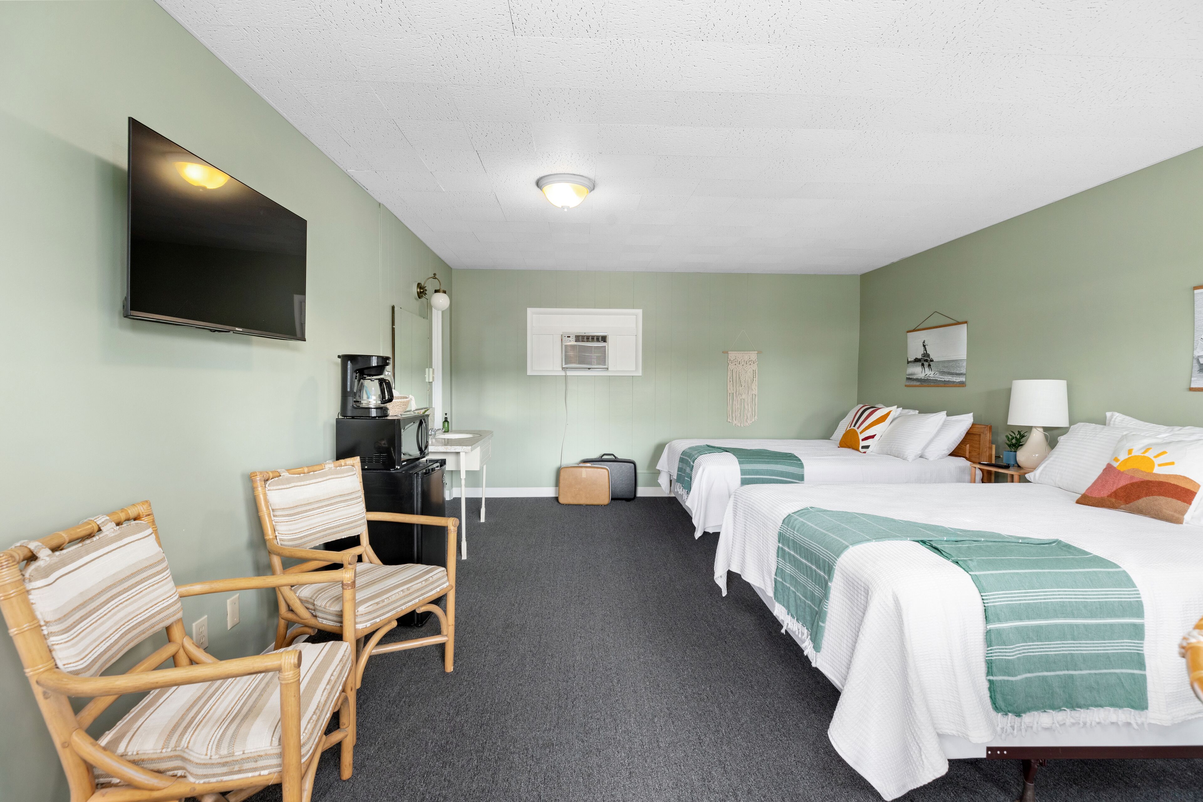 A hotel room with two beds, a TV, a desk with a coffee maker, and a chair.