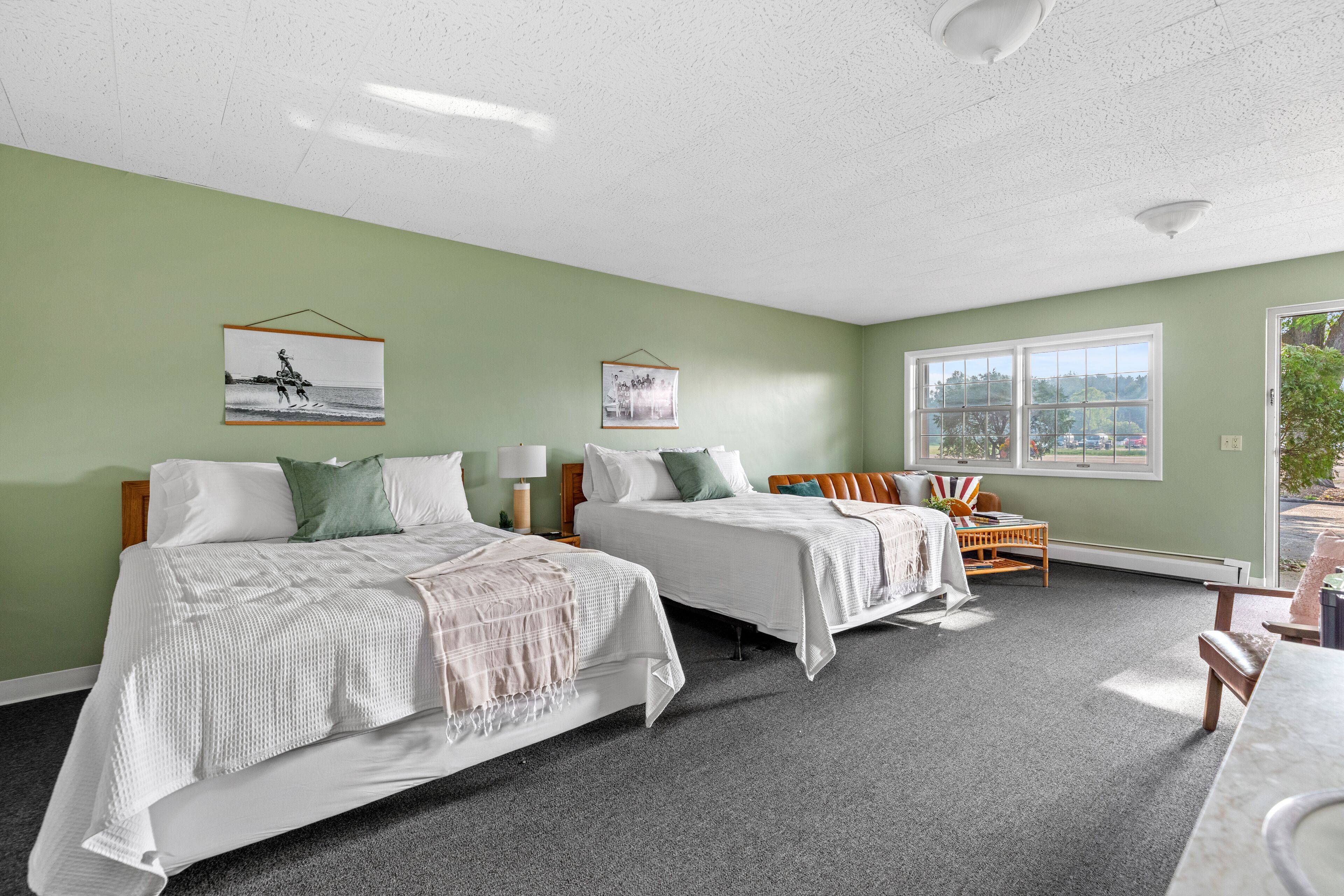 A hotel room with two beds, a small seating area, and large windows.