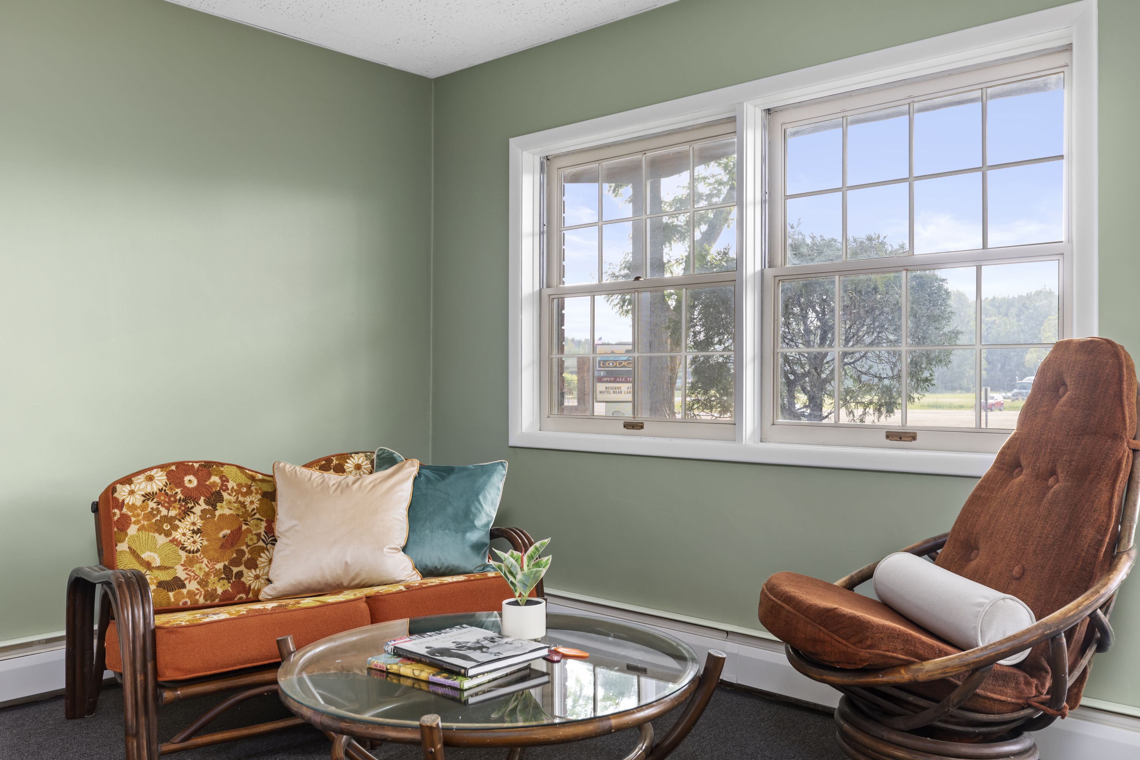 A room with a sofa, a rocking chair, a glass coffee table, and a window with a view of trees.