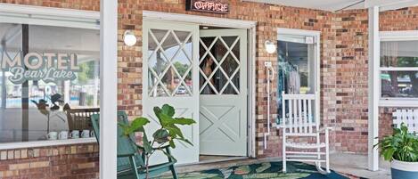 A motel entrance with a brick facade, a sign reading "OFFICE," and a green chair outside.