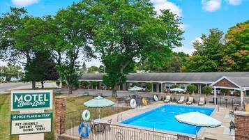 Ein Motel mit Schwimmbad, Sitzgelegenheiten im Freien und einem Schild, das tierfreundliche und Retro-Atmosphäre bewirbt.