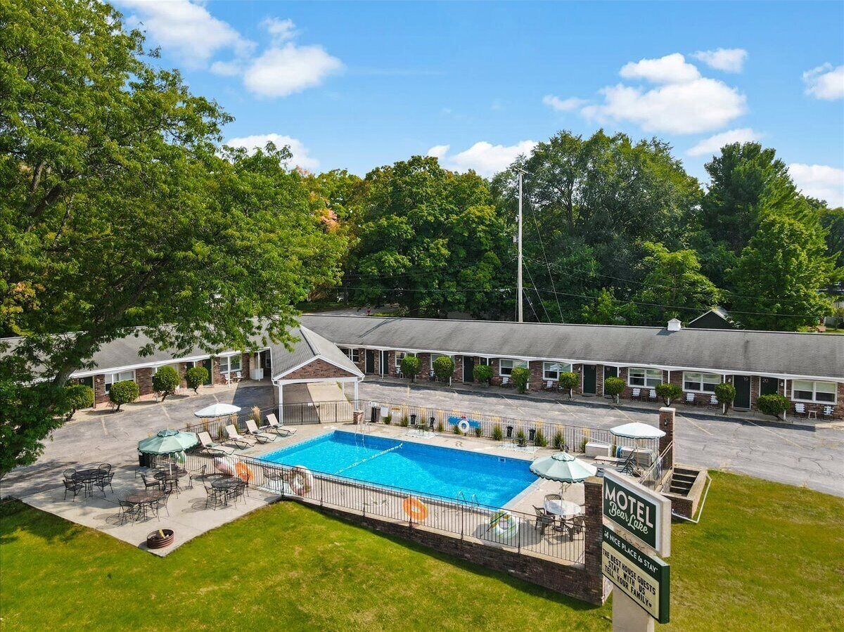 A motel with a swimming pool, outdoor seating, and a covered patio area.