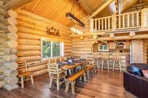 A log cabin interior with a dining area, wooden benches, a kitchen, and a balcony. - Humphreys Peak View Luxury Log Cabin (Fort Valley)