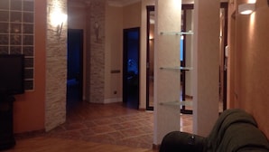A hallway with a stone accent wall, a glass shelf unit, and a television mounted on the wall. - Stylish and new apartments  (Minsk)