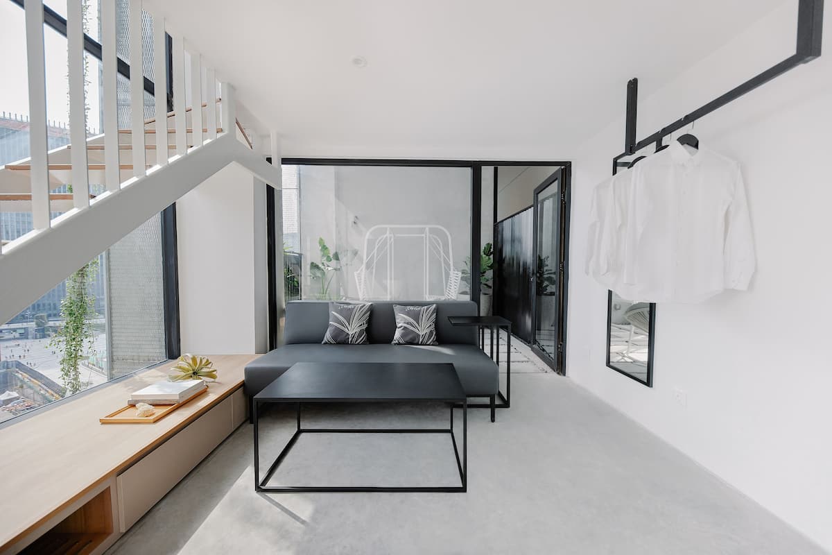 A modern bedroom with a large window, a sofa, a coffee table, and a hanging rack with clothes.
