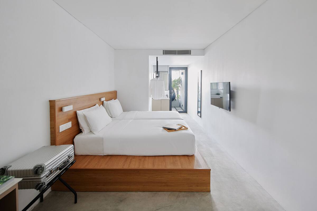 A modern hotel room with a wooden bed, a bedside table with a suitcase, and a TV mounted on the wall.