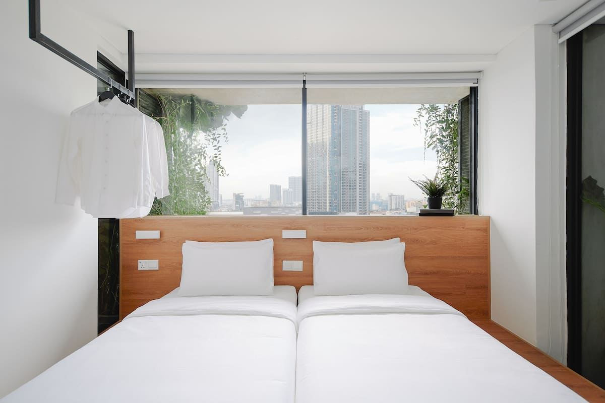 A modern hotel room with a wooden headboard, two white beds, a city view, and a hanging white shirt.