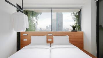 A modern hotel room with a wooden headboard, two white beds, a city view, and a hanging white shirt.