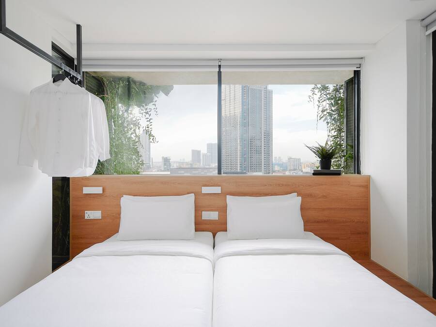 A modern hotel room with a wooden headboard, two white beds, a city view, and a hanging white shirt.
