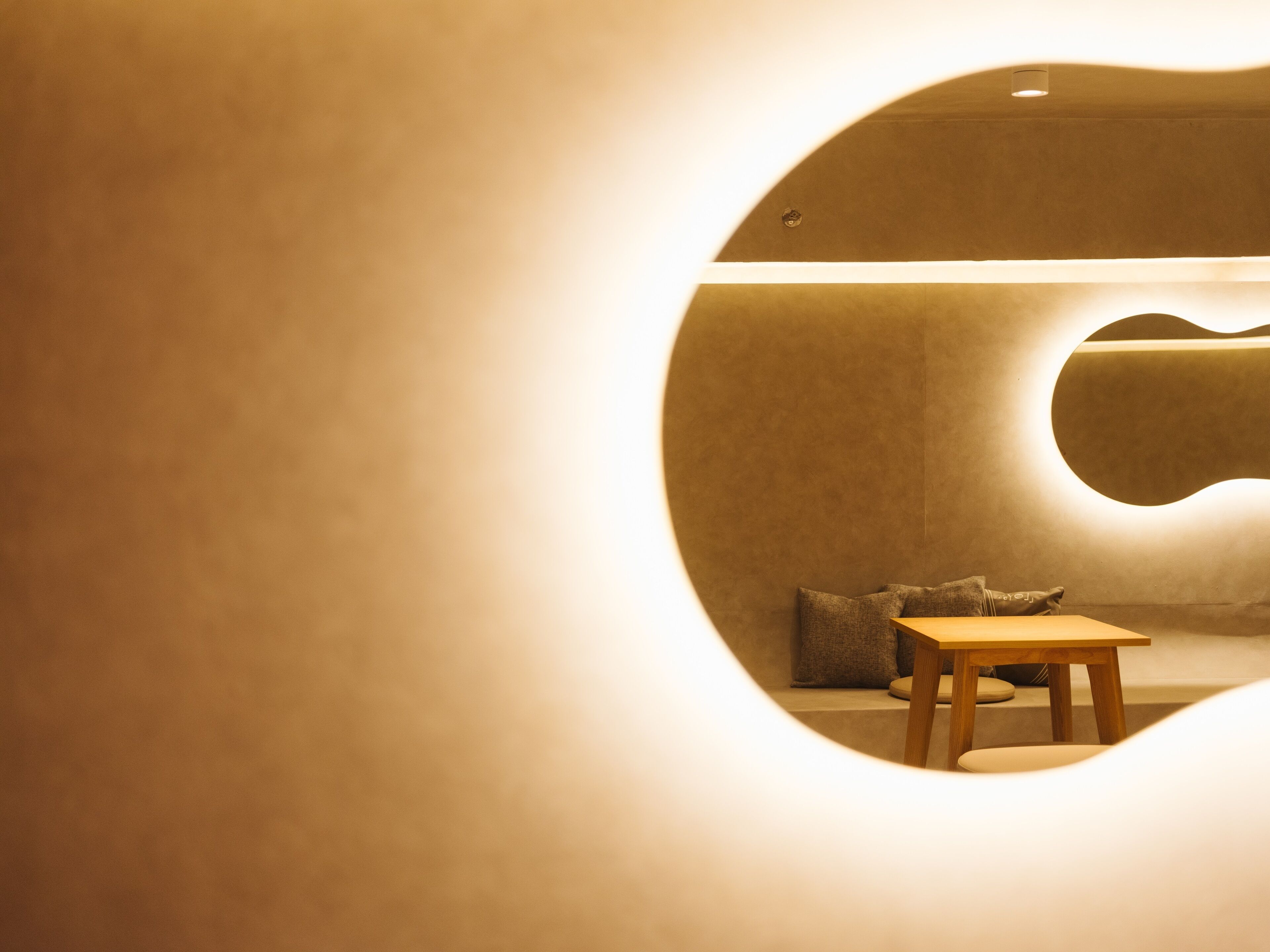 A circular room with a wooden table and a bench, a wall-mounted mirror, and a light fixture.