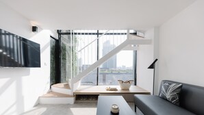 A modern living room with a large window, a staircase, a flat-screen TV, a sofa, and a coffee table. - Lloyd's Inn Kuala Lumpur (Kuala Lumpur)