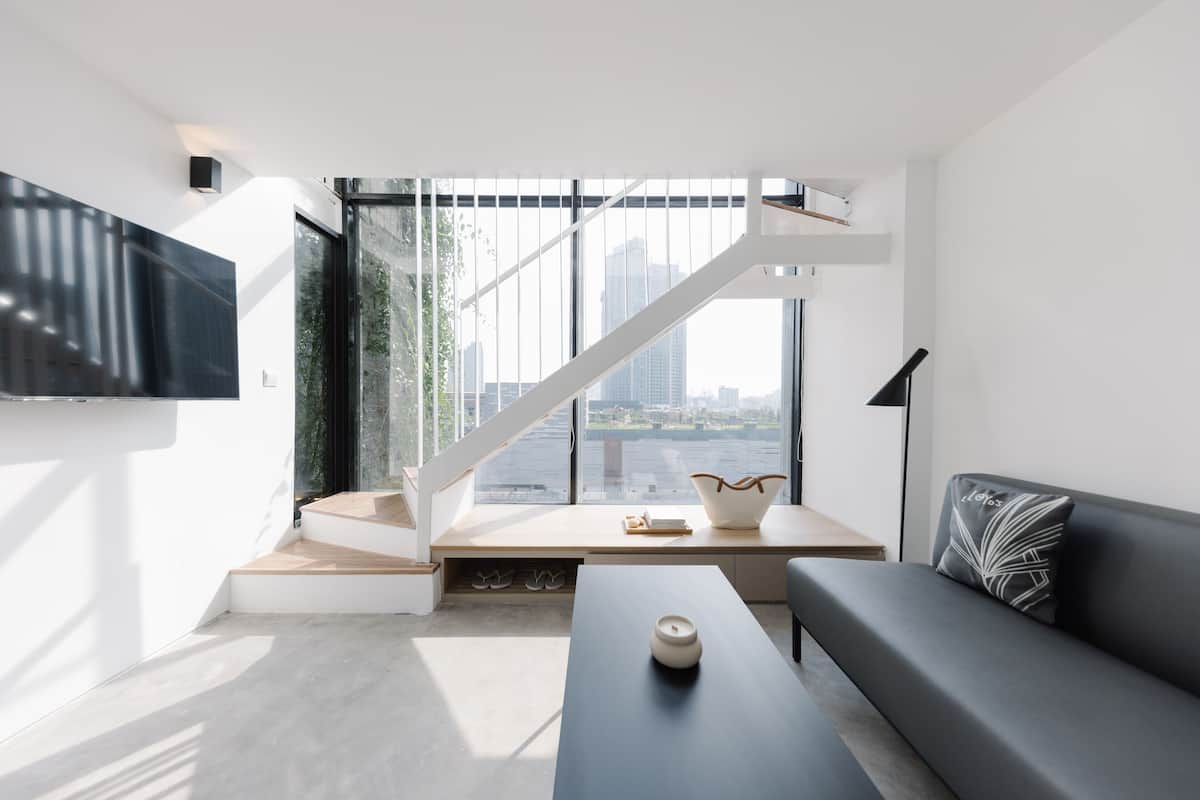 A modern living room with a large window, a staircase, a flat-screen TV, a sofa, and a coffee table.