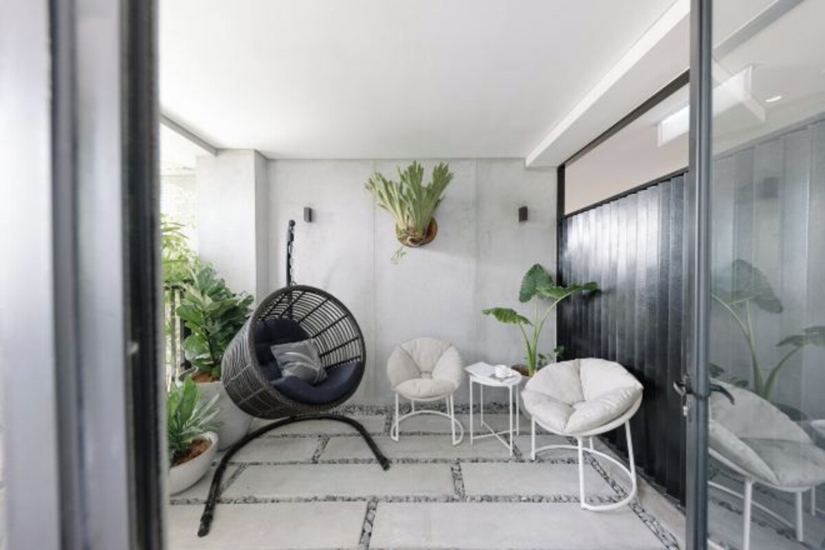 A modern balcony with a hanging chair, two white armchairs, and potted plants.